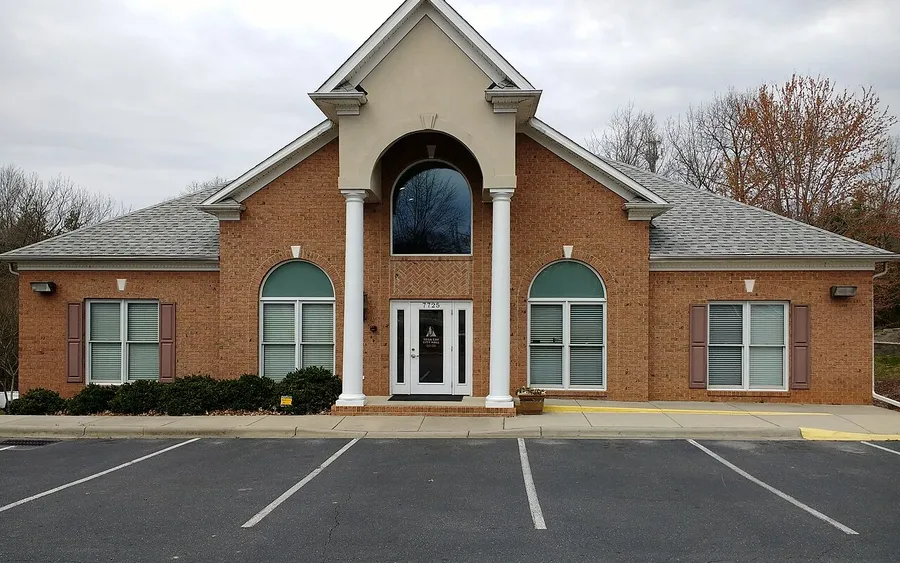 Tega Cay City Hall, a brick building with white columns, an arched center window and green-tinted arched windows, seen across an empty parking lot